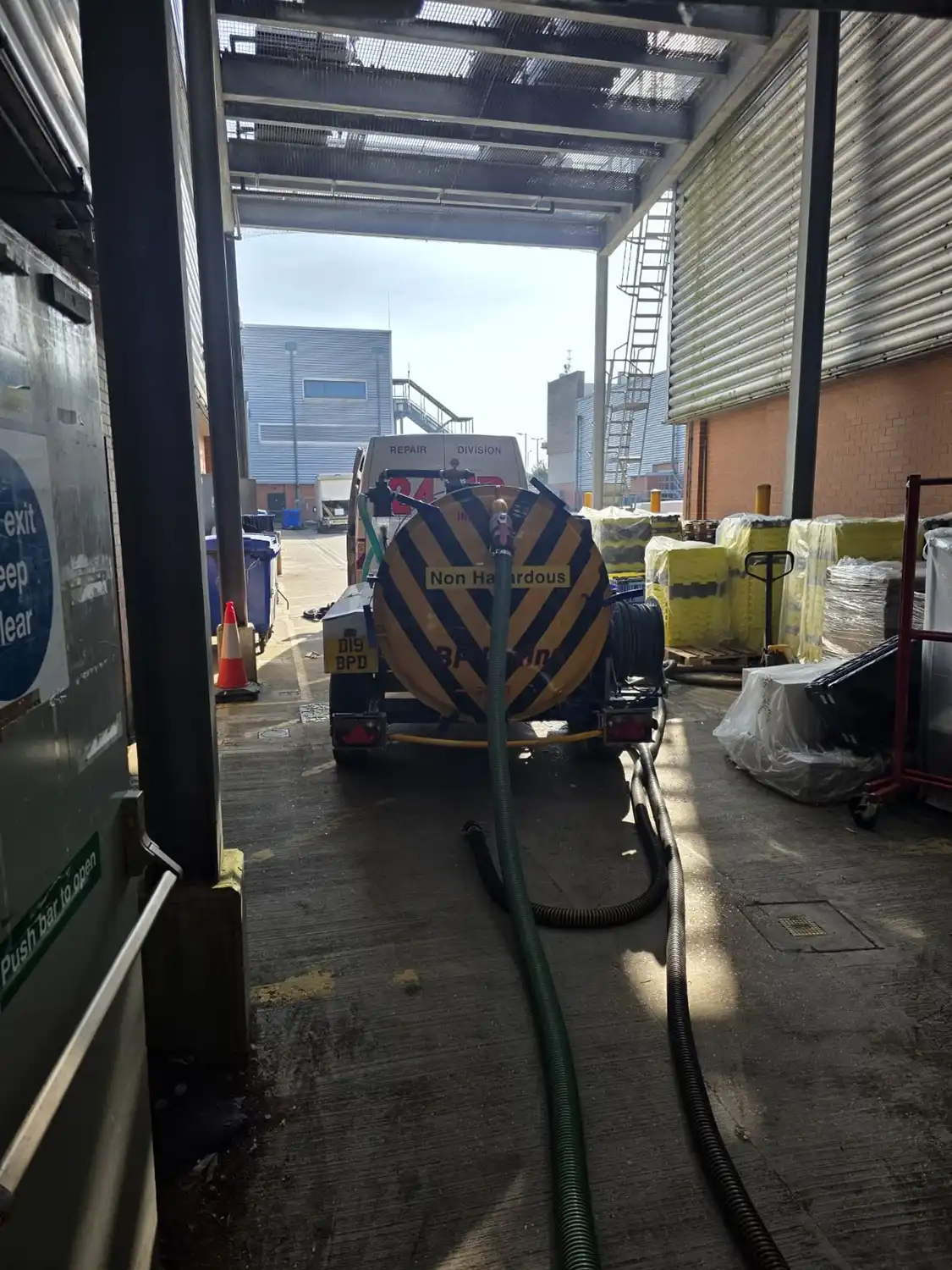 A view of a loading area with a non-hazardous waste truck and hoses, surrounded by warehouse structures and equipment.